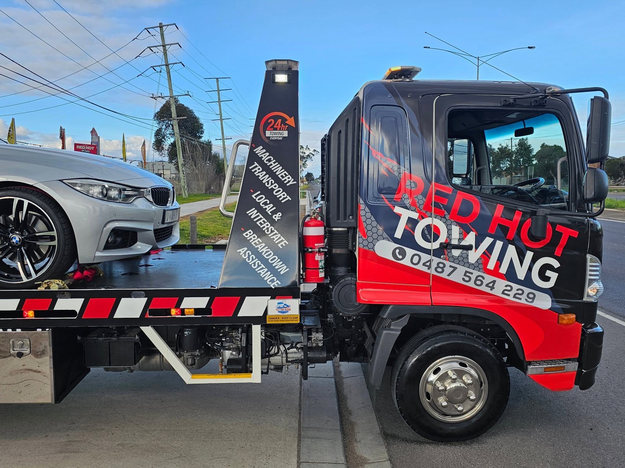 Side view of the Red Hot Towing tilt tray truck with a car loaded